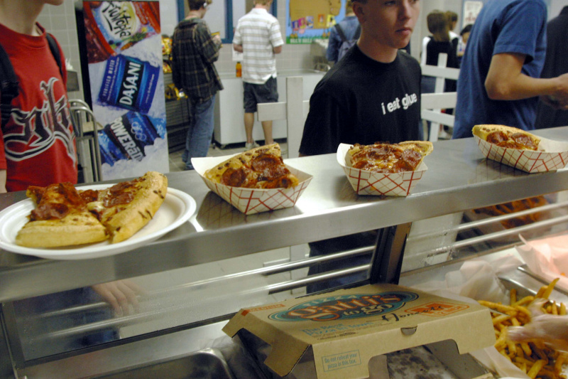   يصطف الطلاب لتلقي الطعام أثناء الغداء في الكافتيريا في مدرسة Bowie الثانوية في 11 مارس 2004 في أوستن ، تكساس. تعمل دائرة مدارس أوستن على جعل عروض الكافتيريا أكثر صحية ، لكن الأطعمة الأكثر شعبية لا تزال شرائح الدجاج المقلي والبيتزا والبطاطس المقلية. جعلت المخاوف بشأن زيادة مستويات بدانة الأطفال في الولايات المتحدة الطعام الذي يتم تقديمه في مقاهي المدارس العامة مصدر قلق أكبر بكثير.